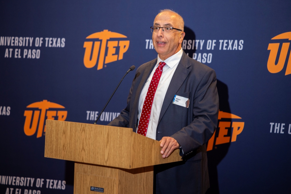 A man in a suit speaks from a podium in front of a UTEP backdrop.
